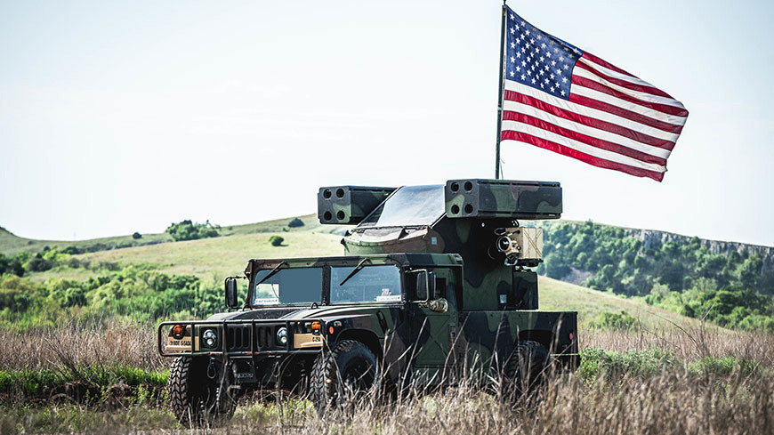 Military vehicle drives outdoors with American flag