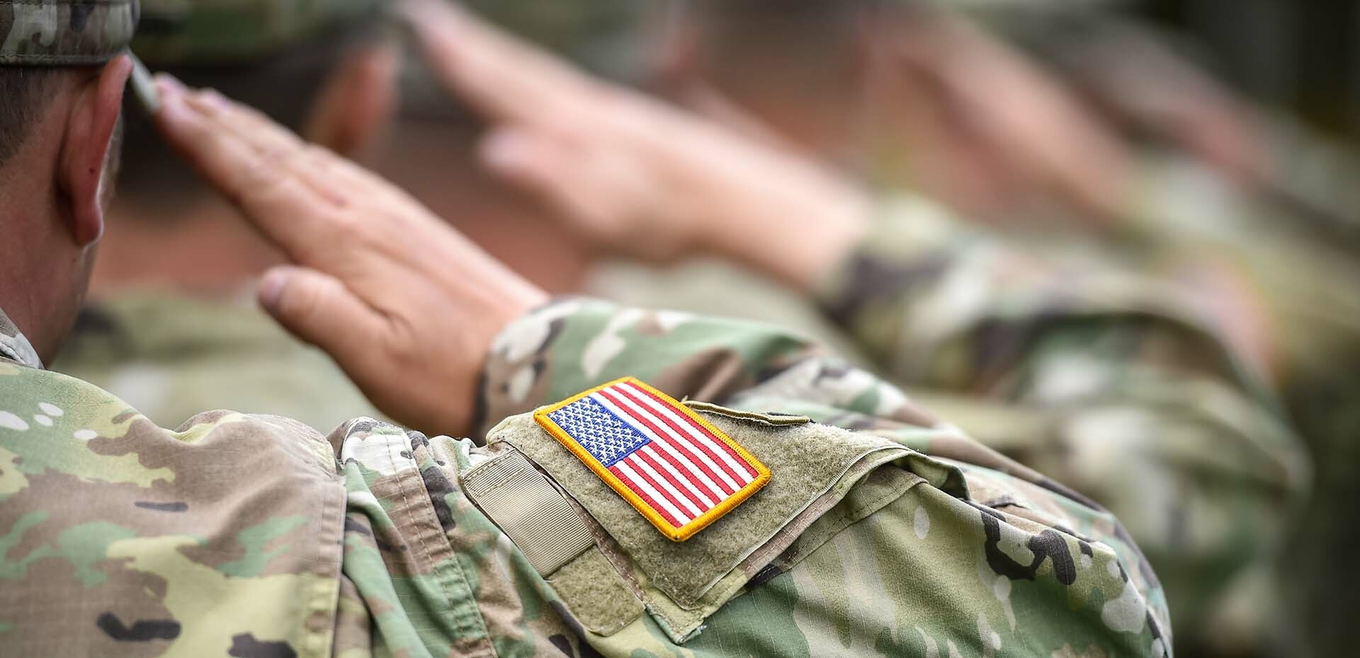 Military man salutes with flag on uniform sleeve